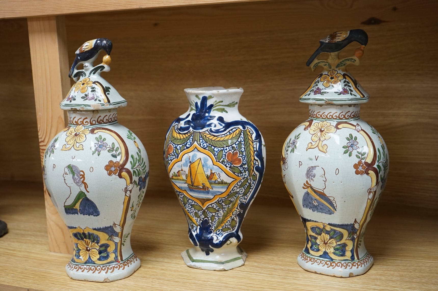 Three 18th/19th century Delft vases, the pair decorated with portraits of king and queen, H 30cm x W 15 (with lids), H 23cm x W 15 (without lid)